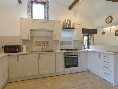 A kitchen with white cabinets a stainless steel oven and hood a microwave and a window at Buster Barn in Sampford Spiney near Tavistock