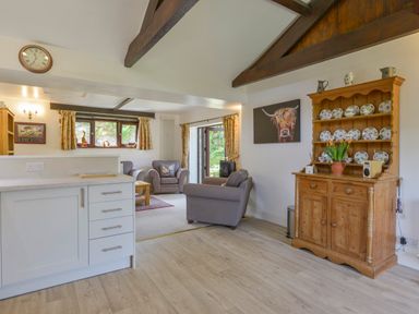 A kitchen and living room with wooden beams a wooden dresser with plates and gray armchairs at Buster Barn in Sampford Spiney near Tavistock