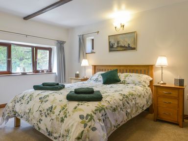 A bedroom with a bed with floral bedding two bedside tables with lamps and a window with curtains at Buster Barn in Sampford Spiney near Tavistock