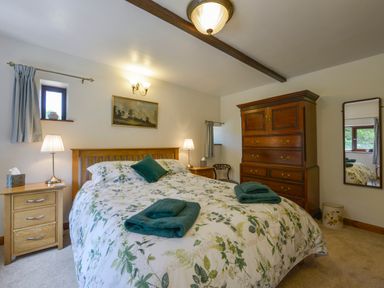 A bedroom with a bed with floral bedding two bedside tables lamps a wooden chest of drawers and a wall mirror at Buster Barn in Sampford Spiney near Tavistock