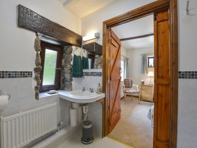 A bathroom with a sink radiator and window next to a bedroom with a chair lamp and bedside table at Buster Barn in Sampford Spiney near Tavistock