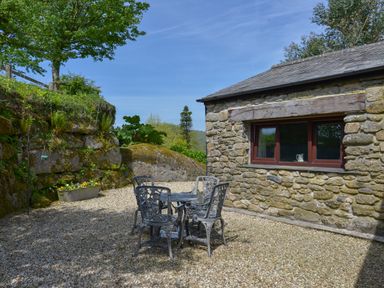 An outdoor seating area with four metal chairs and a table on a gravel surface beside a stone building at Buster Barn in Sampford Spiney near Tavistock