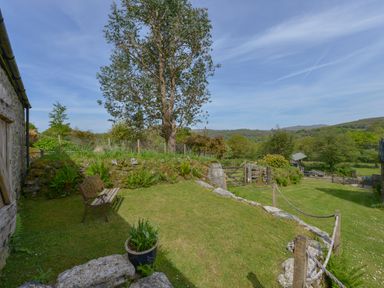 A grassy garden area with a wooden bench and potted plant near a stone wall at Buster Barn in Sampford Spiney near Tavistock