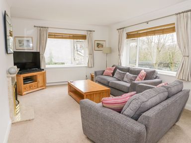 A living room with two gray sofas a wooden coffee table a TV on a stand and windows with curtains at The Dene in Betws-y-Coed
