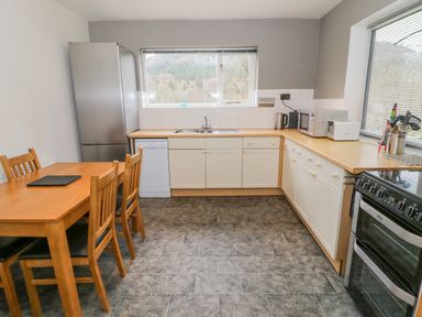 A kitchen with a wooden dining table and four chairs stainless steel refrigerator dishwasher oven microwave kettle and utensils at The Dene in Betws-y-Coed