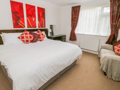 A bedroom with a bed white linens red pillows a dark wooden desk mirror and window with curtains at The Dene in Betws-y-Coed