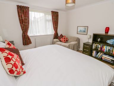 A bedroom with a bed and cushions a sofa with cushions a bookshelf and a window with curtains at The Dene in Betws-y-Coed