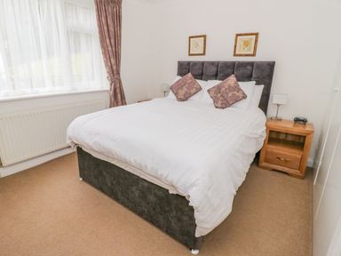 A bedroom with a double bed and two pillows next to a window with curtains at The Dene in Betws-y-Coed