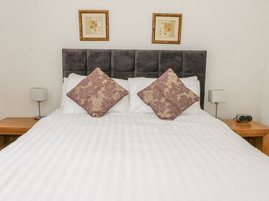 A bed with two floral cushions two bedside tables with lamps and framed pictures on the wall at The Dene in Betws-y-Coed