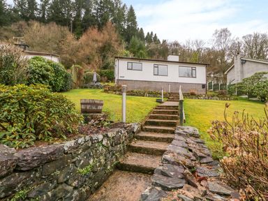 Stone steps leading up through a garden to a single-story house with a brick base at The Dene in Betws-y-Coed