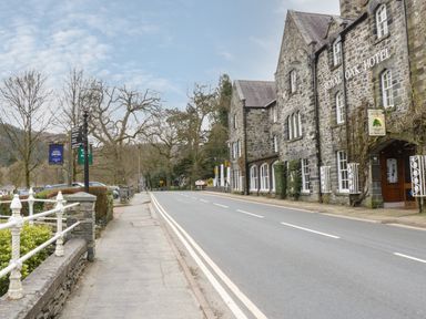 A street view with stone buildings and a road with double yellow lines at The Dene in Betws-y-Coed