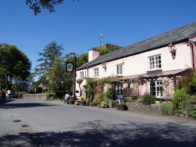A street with a pink building with white windows and outdoor seating with plants at The Linhay in Lydford