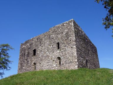 A stone fortress with small windows on a grassy hill under a clear blue sky