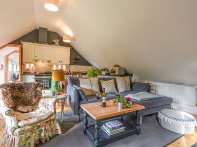 A living area with a floral armchair a gray sofa wooden coffee table and kitchen cabinets at The Linhay in Lydford