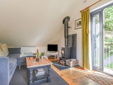 A living room with a wood stove a television a grey sofa and a wooden coffee table at The Linhay in Lydford