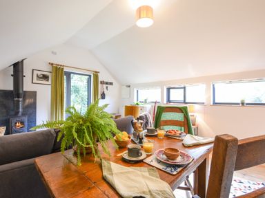 A dining area with a wooden table set for breakfast a fern plant and a fireplace in the background at The Linhay in Lydford