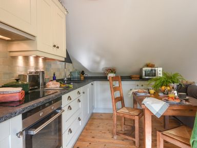 A kitchen with white cabinets wooden chairs and a dining table set for breakfast at The Linhay in Lydford