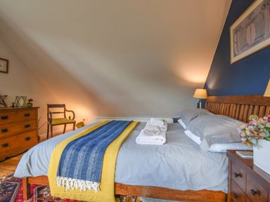 A bedroom with a wooden bed with grey bedding towels on the bed a wooden dresser and a chair at The Linhay in Lydford