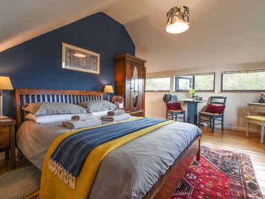 A bedroom with a double bed towels on bed two chairs and a small table near windows and a wardrobe at The Linhay in Lydford