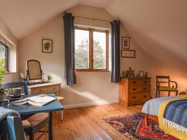 A bedroom with a wooden floor a bed a wooden dresser a chair a vanity table and a blue table with a book at The Linhay in Lydford