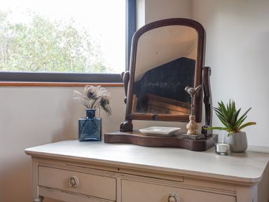 A wooden framed mirror on a white dresser with a blue vase holding peacock feathers a small dish a bird figurine a succulent plant and a candle at The Linhay in Lydford