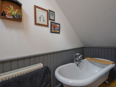 A bathroom with a white clawfoot bathtub wooden tray towel on rack and framed pictures on wall at The Linhay in Lydford