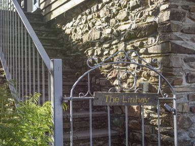 A metal gate with a sign reading The Linhay in front of stone steps and a stone wall at The Linhay in Lydford