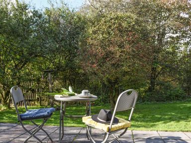 A garden patio with a metal table and two chairs with cushions and a hat on one chair at The Linhay in Lydford
