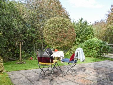 A patio with two chairs and a small table in a garden with bushes at The Linhay in Lydford