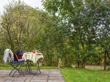 A small patio with a table and two chairs beside grass and trees at The Linhay in Lydford