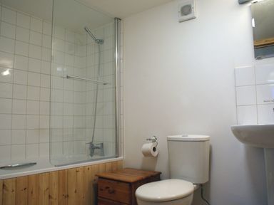 A bathroom with a bathtub and shower, toilet, wooden cabinet, and sink at The Stone Barn Cottage in Holne