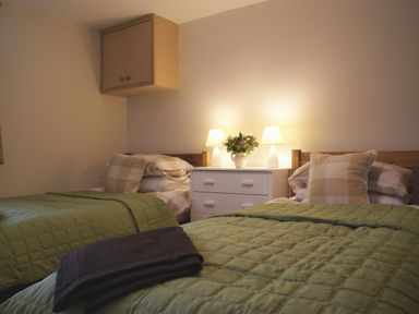 A bedroom with two single beds green bedspreads and a white dresser with two lamps and a vase at The Stone Barn Cottage in Holne