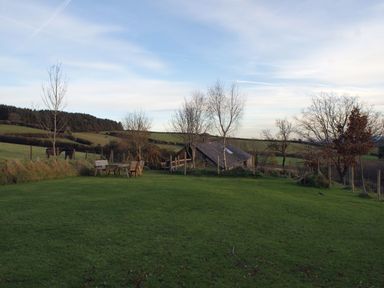 An outdoor grassy area with wooden chairs and table trees and a small building in the background at The Stone Barn Cottage in Holne