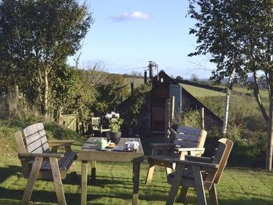 A garden with wooden chairs and a table with a teapot and flowers outside a stone building at The Stone Barn Cottage in Holne