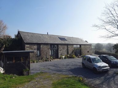 A stone barn building with cars parked outside and potted plants near the doors at The Stone Barn Cottage in Holne
