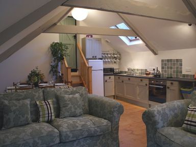 A kitchen and living area with a staircase a fridge and patterned sofas at The Stone Barn Cottage in Holne