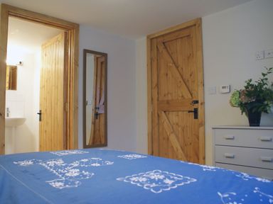 A bedroom with wooden doors a blue patterned bedspread a white dresser and a mirror on the wall at The Stone Barn Cottage in Holne
