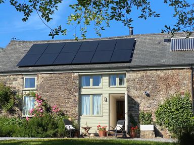A stone cottage with solar panels on the roof and two chairs with a small table outside at The Stone Barn Cottage in Holne