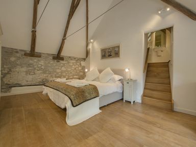 A bedroom with a bed next to two nightstands and wooden stairs leading to a small bathroom at Cullaford Cottage in Scorriton near Ashburton