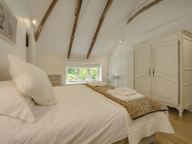 A bedroom with a bed towels on a blanket a wardrobe and wooden ceiling beams at Cullaford Cottage in Scorriton near Ashburton