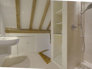 A bathroom with a wall-mounted sink shower area wooden beams on ceiling and storage shelves at Cullaford Cottage in Scorriton near Ashburton