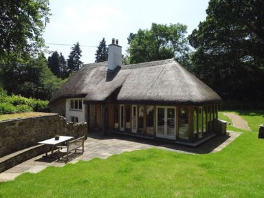 A thatched cottage with stone walls patio table and bench on grass at Cullaford Cottage in Scorriton near Ashburton