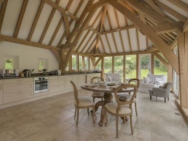 A kitchen and dining area with wooden beams a round dining table four chairs a sofa and an armchair at Cullaford Cottage in Scorriton near Ashburton