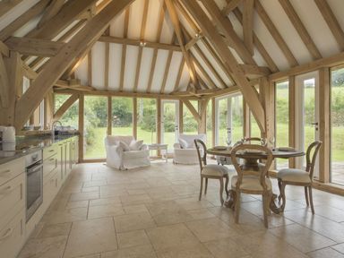 A kitchen dining area with wooden beams large windows and doors two armchairs and a round dining table with four chairs at Cullaford Cottage Scorriton near Ashburton