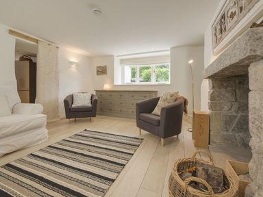 A living room with two armchairs a sofa a striped rug a stone fireplace and a sideboard under a window at Cullaford Cottage in Scorriton near Ashburton