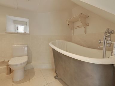 A bathroom with a toilet and a freestanding clawfoot bathtub with a towel on the rim at Cullaford Cottage in Scorriton near Ashburton