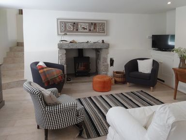 A living room with a fireplace three armchairs a striped rug and a television at Cullaford Cottage in Scorriton near Ashburton