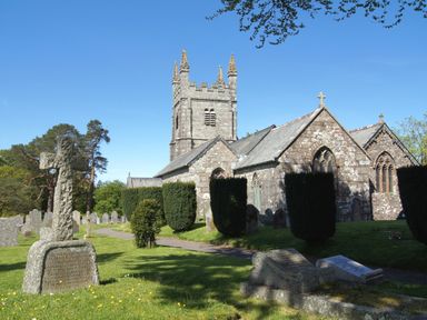 A stone church with a tower surrounded by gravestones and trimmed hedges under a blue sky at Townend Barn in Lydford