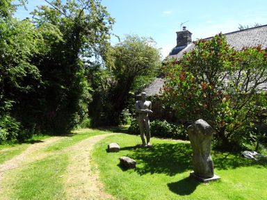A grassy yard with two stone sculptures near a house and trees at Townend Barn in Lydford
