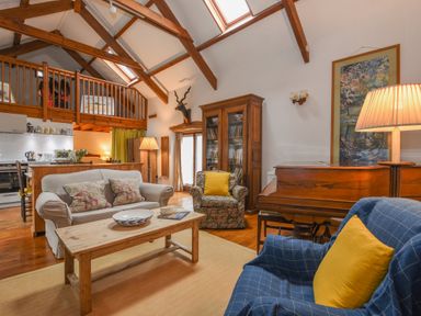 A living room with wooden beams a sofa armchairs a coffee table a piano and a wooden bookshelf at Townend Barn in Lydford